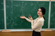 © RomanR - young pretty teacher learn lesson on chemistry and standing near blackboard with chemical formula