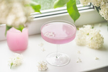 Fresh Pink Non Alcoholic Cocktail In Glass With Lilac Flowers Against Window Background.