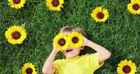 Canvas Print - Happy child lying on green grass amid sunflowers. Slow motion