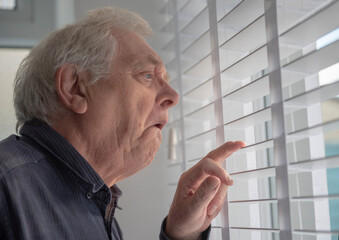 Senior man with funny facial expression looking out of window blinds 