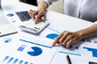 © kamiphotos - Businesswoman using a white calculator, a financial businessman examining the numerical data on a company financial document, she uses a calculator to verify the accuracy of numbers.