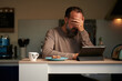 © Enadan - tired man eating breakfast in his kitchen at dawn while looking at his digital tablet with his hand over his face