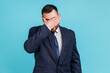 Portrait of young adult wearing official style suit closing eyes with hand, dont want to see that, ignoring problems, hiding from stressful situations. Indoor studio shot isolated on blue background.