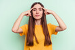 © Asier - Young caucasian woman isolated on green background focused on a task, keeping forefingers pointing head.