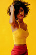 © Carlos David - beautiful young African american woman in bright summer outfit posing isolated on yellow background
