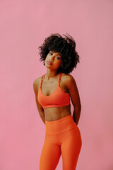 Wall Mural - attractive young black african american adult woman in sports outfit looking at camera and posing isolated on pink background