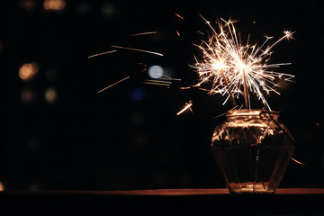 Wall Mural - Bengal lights in glass jar against background of  busy night city. Festive sparklers at night.