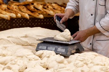 Baker weighing dough portions for baking buns at the manufacturing. Man weighing raw dough on scale in bakery.