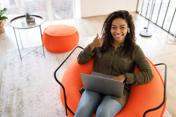 Wall Mural - Portrait of smiling black woman using laptop showing thumbs up