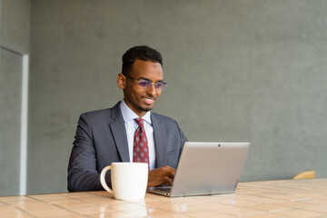 Wall Mural - African businessman wearing suit and tie in coffee shop while using laptop computer