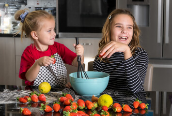 Little girls play chefs. Two sisters enthusiastically cook strawberry cookies in the kitchen.