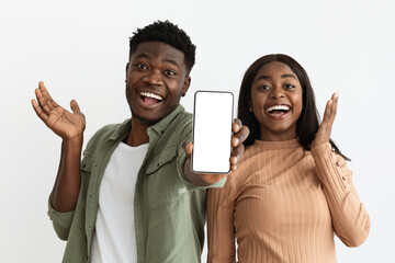 Emotional african american couple showing smartphone with empty screen, mockup