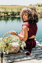 Black Woman Sits On Dock While Holding Basket Full Of Wildflowers