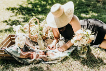 Woman Lays On Blanket Surrounded By Picnic, Flowers, And Wine