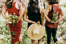 Group Of Women Stand In Forest Holding Flowers Behind Backs