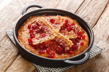 Traditional delicious Swedish egg pancake Aggakaga with crispy bacon and cranberries close-up in a frying pan on the table. horizontal