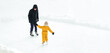 Father and baby are standing on the ice rink opposite each other. Dad teaches his daughter to skate outdoors on a cold day. Active entertainment during the winter holidays.