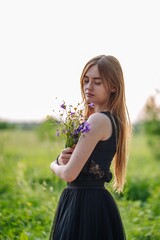 Portrait of a Russian girl with a bouquet of wild flowers in the evening at the village.