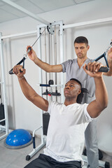 Wall Mural - Male working out at gym supervised by physiotherapist