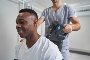 Wall Mural - Pleased patient having his neck massaged with percussion gun