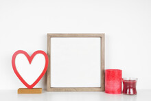 Mock Up Square Wood Frame With Valentines Day Blank Heart Sign And Candles. White Shelf Against A White Wall. Copy Space.