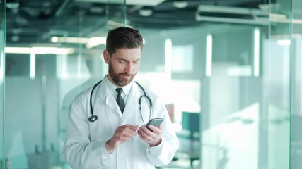 doctor uses mobile smart phone while standing in a modern hospital clinic. male medic using smartpho