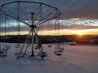 Abandoned and empty carousel on the top of mountain covered with snow on winter dusk with beautiful colorful sky