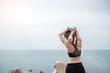 Young fitness female in sportswear stretching body against ocean view, healthy woman exercise in morning. Workout, wellness and work life balance concepts