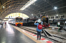 At Hua Lamphong Railway Station Tourists Wear Long-sleeved Shirts. Red Backpack, Green Hat, Mobile Phone To Capture The Impression Of The Ancient Steam Locomotive Train 850, Thailand, 