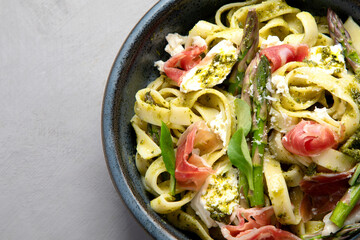 Pasta with asparagus and prosciutto on gray background.