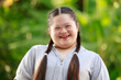 Portrait shot of Asian young chubby down syndrome autistic autism little cute schoolgirl with braid pigtail hairstyle model stand posing smiling look at camera in front blurred garden view background