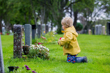 Sad little child, blond boy, standing in the rain on cemetery, sad person, mourning