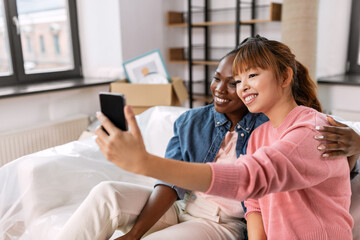 moving, people and real estate concept - happy smiling women with smartphone taking selfie at new home