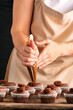Pastry-cook hand prepare chocolate cupcakes. Vertical frame. Woman decorates muffins with cocoa cream in her kitchen.