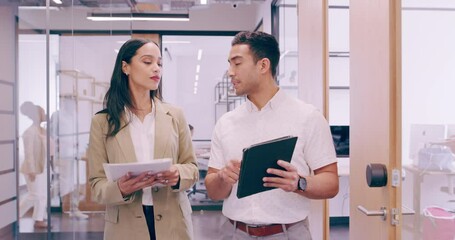 Confident businessman and businesswoman talking while walking in a modern office. Two colleagues brainstorming and using a digital tablet in a work space. Young man sharing an idea with his boss. 