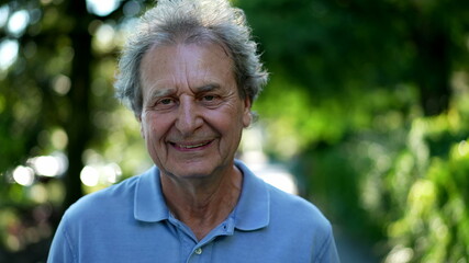 Smiling senior man walking outside in green path, one happy older person