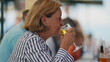 © Marco - Senior woman drinking glass beer seated at restaurant. Older lady takes a sip of refreshing beverage