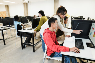 Teacher working with students inside computer class room - Focus on asian guy face