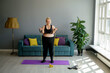 An obese overweight woman does an exercise using an expander. A fat woman in a sports top and leggings does an workout at home in the living room
