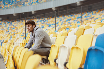 Wall Mural - Sportsman sitting on seat on stadium in earphones