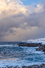 Wall Mural - winter sea with snow covered rocky shores and a small lighthouse on a promontory in the distance