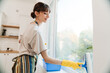 © Drobot Dean - White young woman in gloves smiling while cleaning window