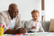 Black Little Boy And His Grandfather Sketching Together At Home