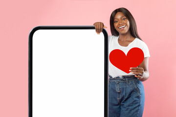 Black woman showing white empty smartphone screen holding paper heart