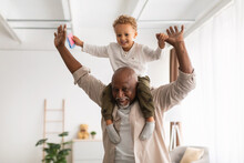 Cheerful Black Grandpa Carrying Little Grandson On Shoulders Playing Indoor