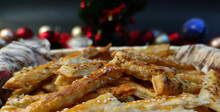 Close-up View Of Puff Pastry Salty Sticks Sprinkled With Cumin And Sesame Seeds, With Christmas Decorations In The Background