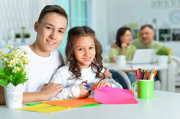 Wall Mural - Portrait of brother and sister sitting at table and spending time together