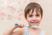 A Smiling Boy Is Brushing His Teeth In The Bathroom. Oral Hygiene.