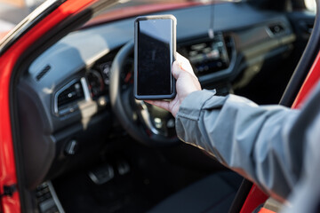 Woman using smartphone in front of the car. Communication or connect to an app. Car sharing, rental service or taxi app
