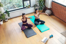 Two Sporty Young Women Doing Exercises Following Online Gym Classes Via Laptop On Floor At Home.